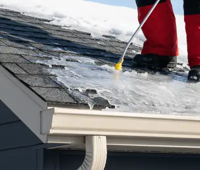 Ice dam removal technician using a steam wand to melt thick ice buildup on a residential roof in Aurora, CO