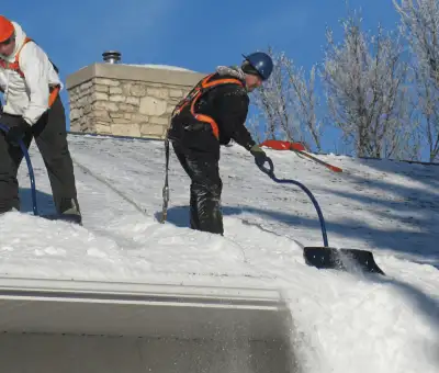 Professional technicians performing roof snow removal with safety harnesses and shovels in Aurora, CO